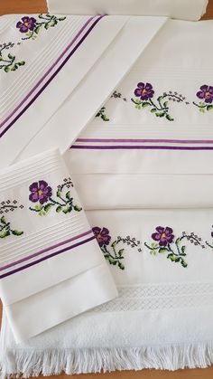 purple flowers are embroidered on white linens