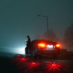 a man standing next to a car with red lights on it