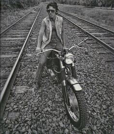 a man sitting on top of a motorcycle next to train tracks