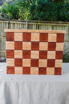 a wooden chess board sitting on top of a white cloth covered table in front of a fence