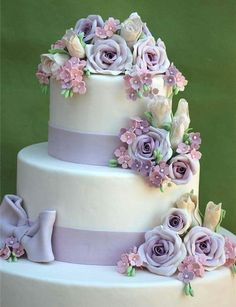 a three tiered white cake with purple flowers on top and ribbons around the edges