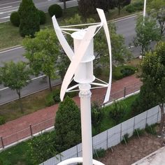 a large white sculpture sitting on top of a metal pole next to a road and trees