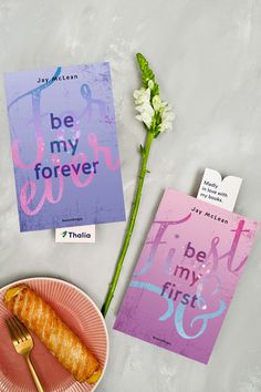 a pink plate with a fork next to a book and a flower on a table