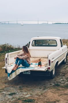 a woman sitting on the back of a white pickup truck next to a body of water