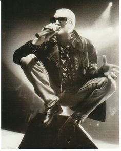 a man sitting on top of a stool while holding a microphone in his hand and wearing sunglasses