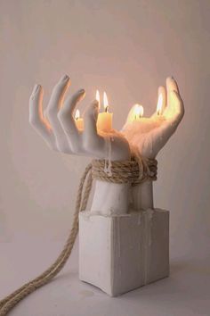 a white sculpture with candles in it and rope wrapped around the base, on a light grey background