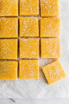 several squares of yellow cake sitting on top of a white tablecloth covered in powdered sugar