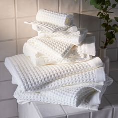 a stack of folded white towels sitting on top of a tiled counter next to a potted plant