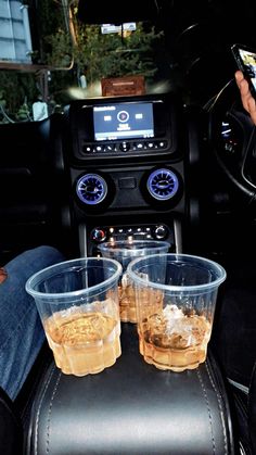 two plastic cups sitting on top of a seat in the back of a car next to a person holding a cell phone