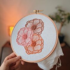 someone holding up a hand embroidered flower on a piece of cloth in front of a lamp