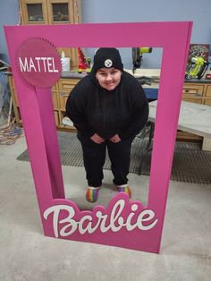 a woman standing in front of a pink frame with the word barbie written on it