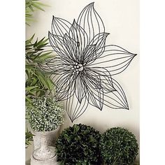 a metal wall hanging with a flower on it next to potted plants and greenery