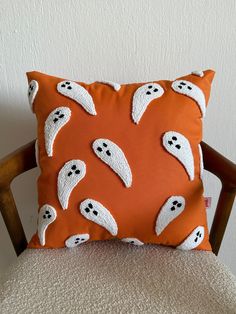 an orange pillow with white ghost faces on it sitting on top of a wooden chair