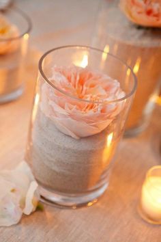 candles and flowers on a table with sand in glass vases for centerpieces