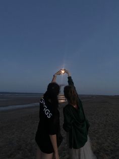 two women standing on top of a sandy beach holding up their hands in the air