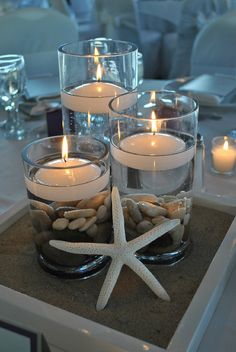 some candles are sitting in glass bowls with rocks and starfish on the bottom one