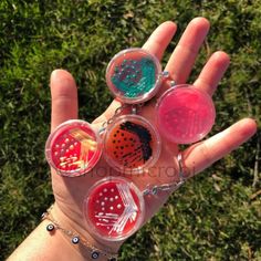 a person holding four different colored objects in their hand with grass in the back ground