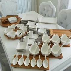 a white table topped with lots of plates and bowls on top of wooden trays