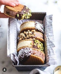 a person holding a piece of bread with chocolate and nuts on it in a box