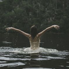 a woman standing in the water with her arms spread out and hands outstretched above her head