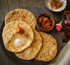 three flat breads on a wooden plate with some sauce and flowers in the background