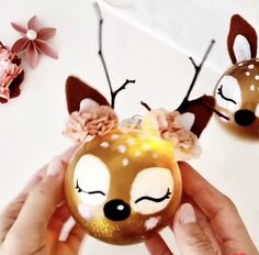 a person holding a christmas ornament with two deer heads on it's head