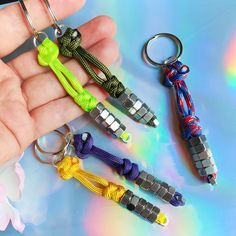 a hand holding four different colored keychains on top of a blue and green table