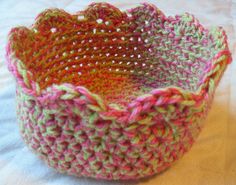 a crocheted basket sitting on top of a white table covered in pink, green and yellow yarn