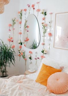 a white bed topped with pink flowers next to a mirror and potted plant on the wall