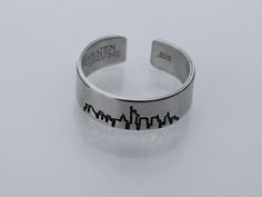 Bring a little piece of New York City wherever you go with this New York City skyline ring, featuring a detailed skyline of New York City. Product Details: Materials: Aluminum, Sterling Silver, Fine Silver, 14k Gold Filled Color: Silver, Gold, Rose Gold Size: 6mm You will receive one hand-stamped ring filled with a black enamel finish. Skyline Ring, Hand Stamped Ring, Stamped Ring, New York City Skyline, Stamped Rings, City Skyline, Black Enamel, Fine Silver, Gold Rose