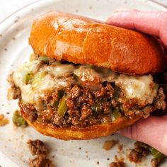 a hand holding a sandwich on top of a white plate with meat and cheese in it