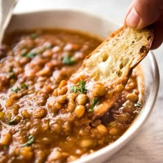 a hand holding a piece of bread over a bowl of beans