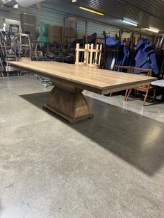 a large wooden table in a warehouse with chairs and tables on the floor behind it