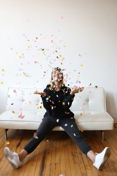 a woman is sitting on a couch with confetti falling from her head and arms