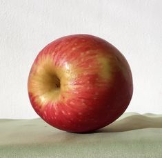 an apple sitting on top of a table next to a white wall and green cloth