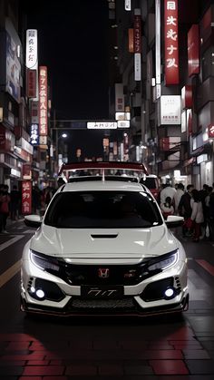 a white car parked on the side of a road in front of tall buildings at night