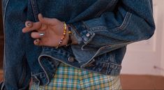 a person wearing a blue jean jacket and colorful bracelets holding their hand in the pocket