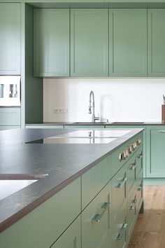 a kitchen with green cabinets and stainless steel counter tops, along with an island in the middle