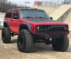 a red jeep parked on top of a dirt field next to a ramp and steps