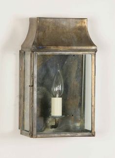 an old fashioned wall mounted lantern with a candle in it's glass case on a white wall