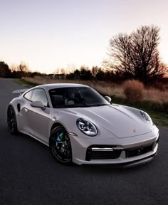 a white sports car parked on the side of a road at sunset or dawn with trees in the background