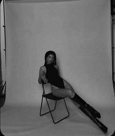 a black and white photo of a woman sitting on a chair with her legs crossed