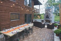 an outdoor dining area with table, chairs and fire place in the back yard is lit by string lights