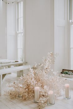 some white flowers and candles are on the floor in front of a bench with windows