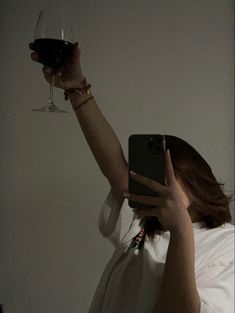 a woman holding up a glass of wine to take a selfie with her cell phone