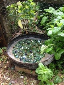 a bucket filled with lots of different colored glass beads sitting in the dirt next to plants