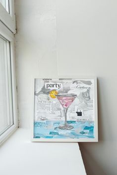 a painting on the side of a window sill next to a white wall with a drink in it