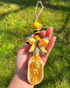 a hand holding a wooden spoon with a bee decoration on it's handle and string