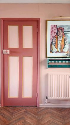 a pink room with two doors and a painting hanging on the wall above it's radiator