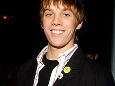 a young man smiles at the camera while wearing a black jacket and white striped shirt